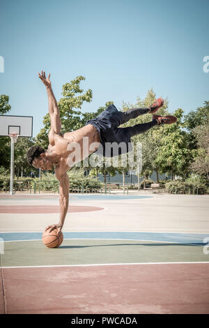 Eine afroamerican junger Mann ohne T-Shirt ist das Gleichgewicht mit einem Basketball in einem Park in Madrid im Sommer mittags. Stockfoto