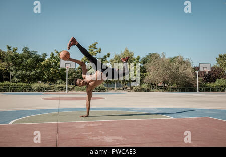 Eine afroamerican junger Mann ohne T-Shirt ist das Gleichgewicht mit einem Basketball in einem Park in Madrid im Sommer mittags. Stockfoto