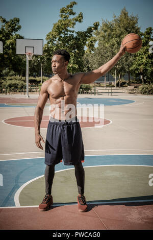 In der Nähe von One afroamerican junger Mann ohne t-shirt Basketball spielen in einem Park in Madrid im Sommer mittags. Er steht und Halten der b Stockfoto