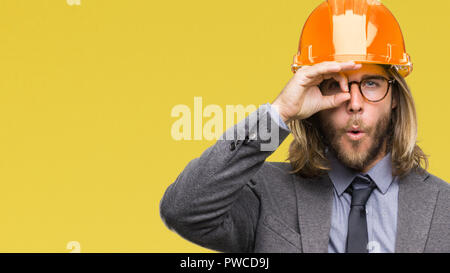 Junge schöne architec Mann mit langem Haar zu tragen Schutzhelm über isolierte Hintergrund tun ok Geste mit Gesicht überrascht, schockiert, Auge. Stockfoto