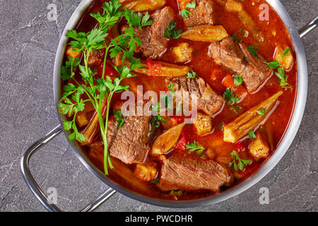 Überblick über herzhaftes Rindfleisch und Okra Eintopf in eine Kasserolle auf einer konkreten Tabelle, Ansicht von oben, flach, close-up Stockfoto