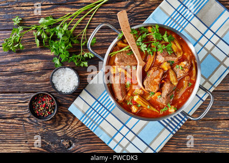 Ansicht von oben der köstlichen Rindfleisch und Baby Okra Eintopf in eine Kasserolle mit Löffel, auf einem alten Holztisch mit Petersilie, Salz und Pfeffer auf t Stockfoto