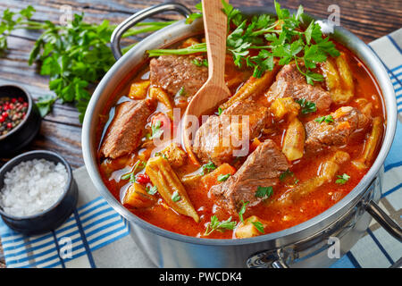 Ansicht von oben der köstlichen Rindfleisch und Okra Eintopf in eine Kasserolle mit Löffel, auf einem alten Holztisch mit Petersilie, Salz und Pfeffer auf der Ba Stockfoto