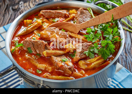 Leckeres Rindfleisch und Okra Eintopf in eine Kasserolle mit Löffel, auf einem alten Holztisch, Ansicht von oben, close-up Stockfoto