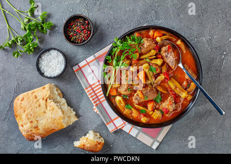 Ansicht von oben der köstlichen Rindfleisch und Okra Eintopf in einer Schüssel mit Löffel serviert, auf einer grauen Beton Tabelle mit Ciabatta Brot, Ansicht von oben, close-up, f Stockfoto