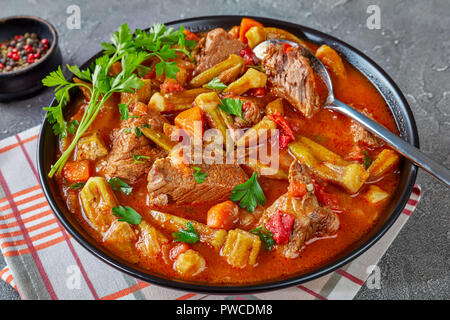 Leckeres Rindfleisch und Okra Eintopf in einer Schüssel mit Löffel serviert, auf einer grauen Beton Tabelle mit Ciabatta Brot, Ansicht von oben, close-up Stockfoto