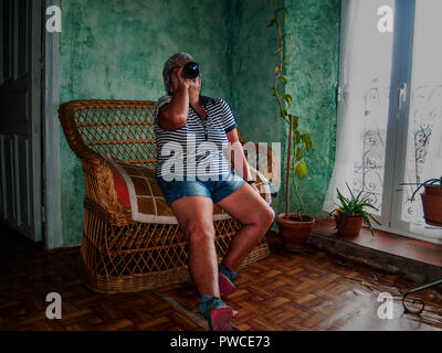 Eine betrunkene Frau trinkt aus einer Flasche Wein in der Hand und sitzt auf einem Sofa Stockfoto