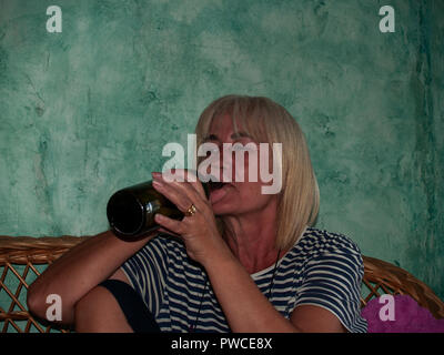 Eine betrunkene Frau trinkt aus einer Flasche Wein in der Hand. Stockfoto