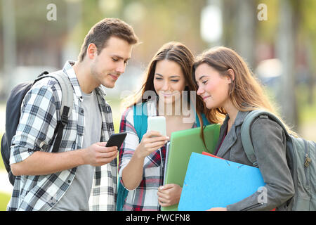 Drei entspannte Schüler beobachten smart phone Inhalt außerhalb in einem Park Stockfoto