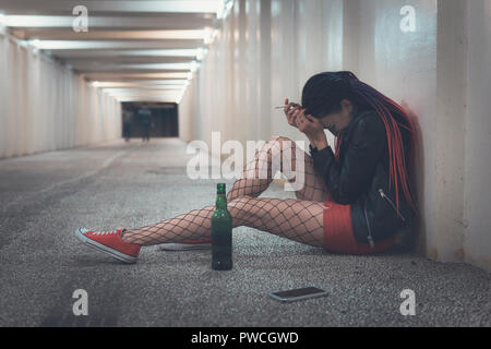 Mädchen erleben Trauer und trinken Alkohol. Frau fühlen, Depressionen und Alkoholismus. Junge betrunkene Mädchen sitzen mit einer Flasche Whisky in der underp Stockfoto