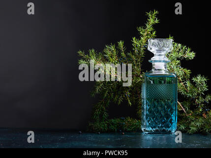 Blue Gin in Kristall Karaffe und Juniper Zweig mit Beeren auf einem schwarzen Hintergrund. Kopieren Sie Platz für Ihren Text. Stockfoto