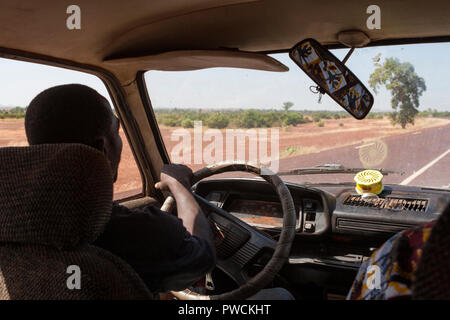 Innenansicht der Afrikanischen Mann, der ein Auto fährt auf einer leeren Straße in der Sahelzone Landschaft Stockfoto