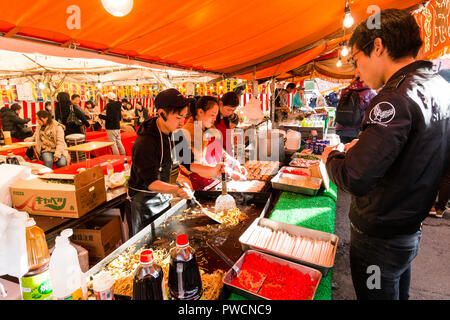 Japanische junge mand und zwei junge Frauen, bei Yakisoba takeaway Kochen gebratene Buchweizennudeln auf Warmhalteplatte während des Festivals. Kunde wartet. Stockfoto