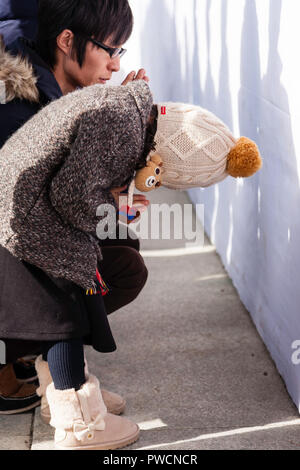 Japanische neues Jahr, shogatsu. Kind, Mädchen, in Bobble hat und gestrickte Mantel Verbeugung betend in der Main Hall, Honden der Nishinomiya Shinto Schrein. Stockfoto