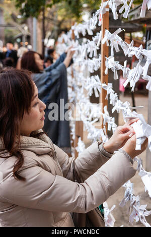 Japanische neues Jahr, shogatsu. Junge Frau binden schlechtes Vermögen Papierstreifen, Omikuji zu rahmen Pech hinter an der Nishinomiya Schrein zu verlassen. Stockfoto