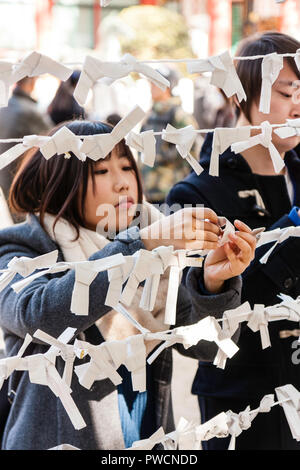 Japanische neues Jahr, shogatsu. Junge Frau binden schlechtes Vermögen Papierstreifen, Omikuji zu rahmen Pech hinter an der Nishinomiya Schrein zu verlassen. Stockfoto