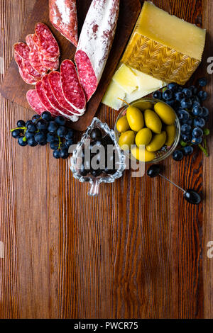 Mix aus verschiedenen Snacks und Vorspeisen. Spanische Tapas auf einer Holzplatte. Tapas Bar. Chorizo, Oliven, Wurst, Käse, Trauben. Ansicht von oben Stockfoto