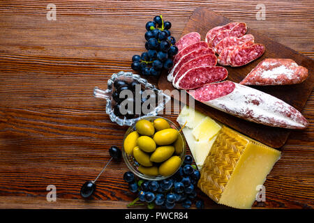Mix aus verschiedenen Snacks und Vorspeisen. Spanische Tapas auf einer Holzplatte. Tapas Bar. Chorizo, Oliven, Wurst, Käse, Trauben. Ansicht von oben Stockfoto