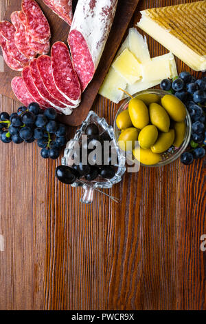 Mix aus verschiedenen Snacks und Vorspeisen. Spanische Tapas auf einer Holzplatte. Tapas Bar. Chorizo, Oliven, Wurst, Käse, Trauben. Ansicht von oben Stockfoto