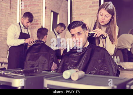 Professionelle friseur Frau tun Styling hübscher Kerl mit elektrischer Haarschneider bei Friseur Stockfoto