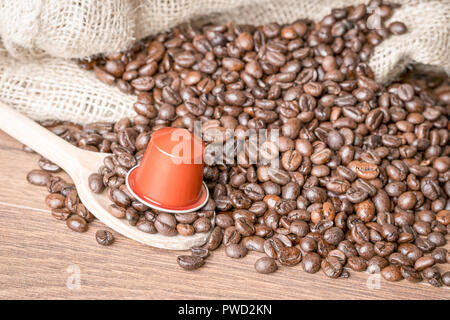 Kaffee Kapsel auf Holzlöffel und geröstete Kaffeebohnen mit sackleinen Sack auf Holz- Hintergrund, aus der Nähe. Stockfoto