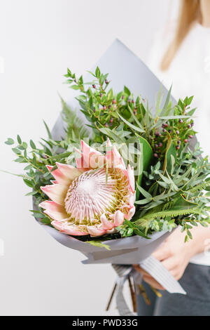 Üppigen Blumenstrauß des Königs Protea, Eukalyptus und andere Grüns. Junge Mädchen, dass eine Blumen Arrangements mit verschiedenen Farben. weiße Wand. Stockfoto