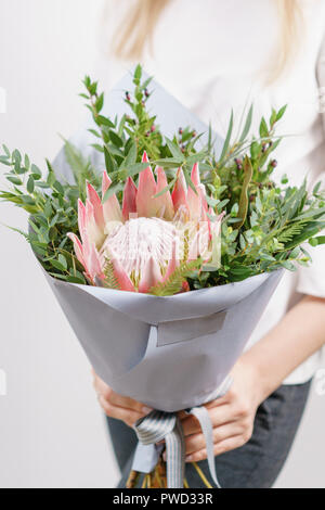 Üppigen Blumenstrauß des Königs Protea, Eukalyptus und andere Grüns. Junge Mädchen, dass eine Blumen Arrangements mit verschiedenen Farben. weiße Wand. Stockfoto