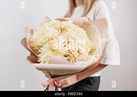 Üppigen Bouquet von seltenen Chrysantheme. Junge Mädchen, dass eine Blumen Arrangements mit verschiedenen Farben. weiße Wand. Stockfoto