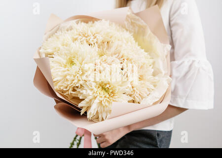 Üppigen Bouquet von seltenen Chrysantheme. Junge Mädchen, dass eine Blumen Arrangements mit verschiedenen Farben. weiße Wand. Stockfoto