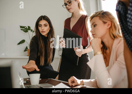 Geschäftsfrau pointing at laptop Bildschirm und zeigt die Informationen zu den weiblichen Kollegen im Büro. Gruppe von Frauen gemeinsam diskutieren mit einem Laptop. Stockfoto