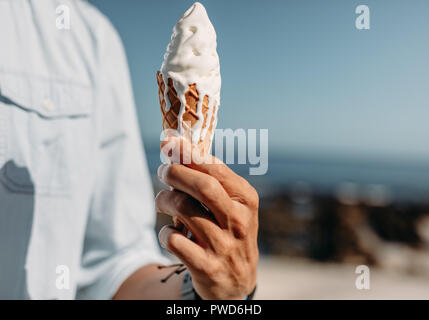 Nahaufnahme der Hand des Menschen mit einem schmelzenden Eis. Mann hält ein Eis an einem sonnigen Tag. Stockfoto