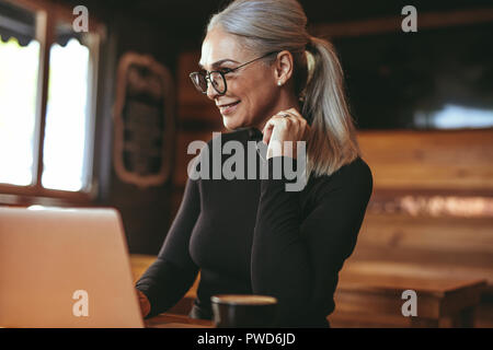Portrait von lächelnden senior Geschäftsfrau. Im Café sitzen und Arbeiten am Laptop. Schöne Frau im Cafe mit Laptop Computer. Stockfoto