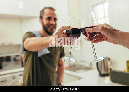 Nahaufnahme von Weingläser angehoben zum Toasten vor dem Trinken. Mann in der Küche zu Hause toasten Wein mit einem Freund. Stockfoto