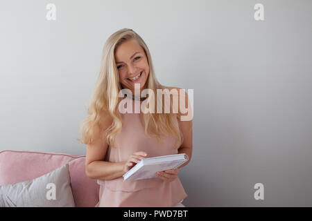 Junge freundliche Frau in einem Stuhl sitzend mit einem Notebook in den Händen. Ein schöner Begleiter. Hellgrauen Hintergrund, kopieren Raum Stockfoto