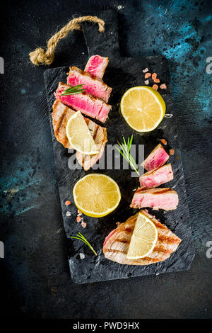 Gegrillter Thunfisch Fisch Steaks mit Zitrone und Gewürze, Dunkelblau konkreten Hintergrund Kopie Raum, Ansicht von oben Stockfoto