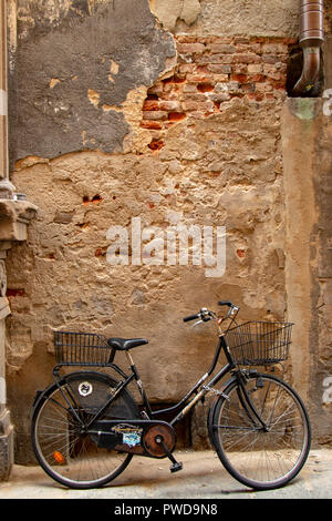 Ein Fahrrad lehnt sich gegen eine alte und verwitterte Wand in einer Gasse in Florenz, Italien. Stockfoto