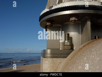 Edelstahl Montageplatte auf Beton mit Edelstahl feste Anker Schrauben, die vertikale Achse Windkraftanlage mit Meer im Hintergrund, Großbritannien Stockfoto