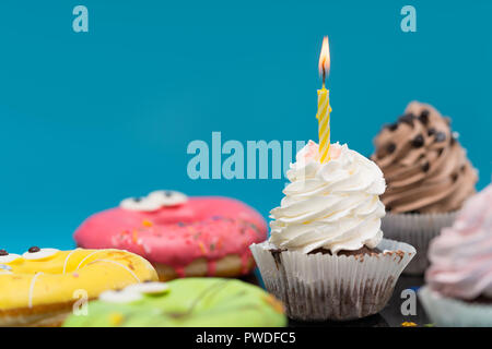 Party Cupcake mit Twirled cremige Vereisung und eine einzelne brennende Geburtstagskerze unter ausgesuchte Kuchen über Blau auf Platz kopieren Stockfoto