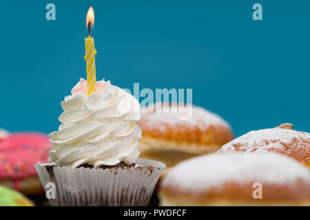 Single Cupcake mit Geburtstag Kerze auf einem Twirl der Vereisung unter frische Sahne Brötchen mit Kopie Raum auf Blau Stockfoto