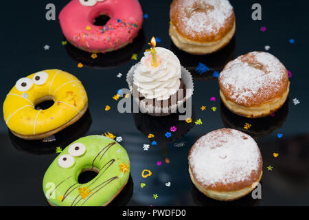 Party Anordnung von frisch gebackenem Kuchen mit Sahne Brötchen, iced Donuts und eine Cupcake mit Kerze gesehen hohen Winkel Stockfoto