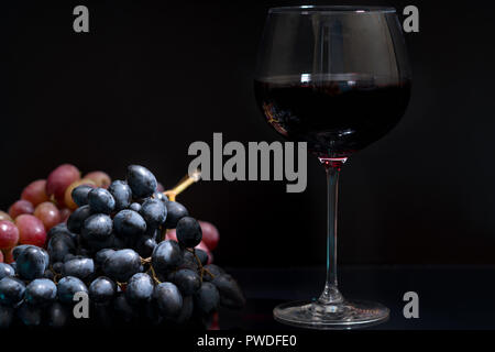 Glas Rotwein neben Trauben von frischen Weintrauben über einen dunklen Hintergrund mit Kopie Raum Stockfoto