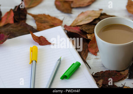 Herbst Konzept. Es gibt Blätter im Herbst, Kaffeetasse, Notebook und Buntstifte sind auf dem Holztisch. Stockfoto