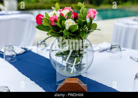 Glas Runde Vase mit bunten Blumenstrauß von bunten Rosen auf dem Tisch bis zum Abendessen. Glas Tisch Nummer vier. Konzept eines tropischen Hochzeit. Stockfoto