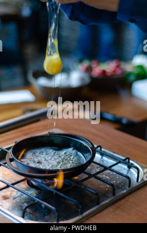 Der Küchenchef brach das Ei in die Pfanne. Eigelb fallen in die Pfanne. Stockfoto