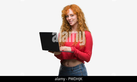 Junge rothaarige Frau mit Computer Laptop mit einem glücklichen Gesicht stehen und lächelnd mit einem selbstbewussten lächeln zähne Stockfoto