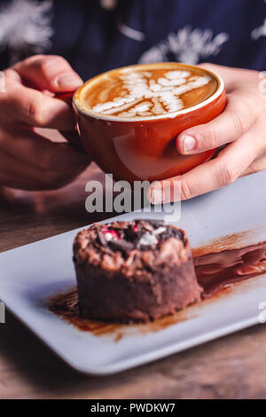 Hände halten Kaffee latte Cup und Schokoladenkuchen auf Tisch Stockfoto
