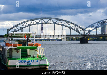 Lettische Eisenbahn Zug vorbei über die Eisenbahnbrücke, Riga, Lettland, über den Fluss Daugava, mit der Radio- und TV-Turm im Hintergrund Stockfoto