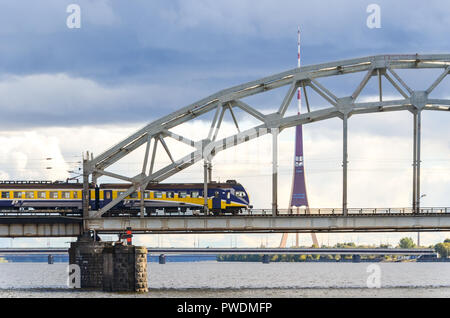 Lettische Eisenbahn Zug vorbei über die Eisenbahnbrücke, Riga, Lettland, über den Fluss Daugava, mit der Radio- und TV-Turm im Hintergrund Stockfoto