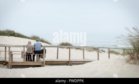 Costa Nova, Portugal - August 2018: Nettes altes Ehepaar in Holzbank sitzen am Meer in Costa Nova Strand suchen. Stockfoto