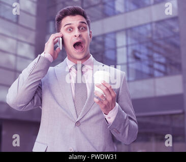 Überrascht Geschäftsmann am Telefon sprechen im Freien mit Einweg Becher in der Hand Stockfoto